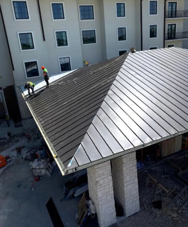 Crew installing standing seam metal roof panels on a commercial project in Elk City